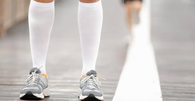 A pair of calves in running shoes wearing compression stockings for vein compression therapy