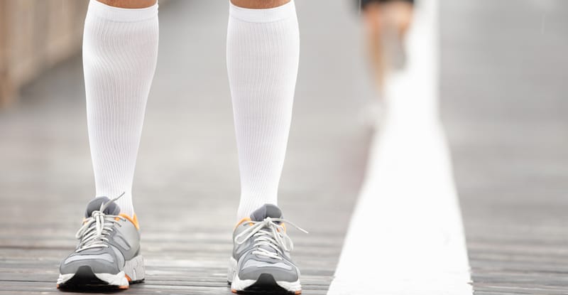 A pair of calves in running shoes wearing compression stockings for vein compression therapy