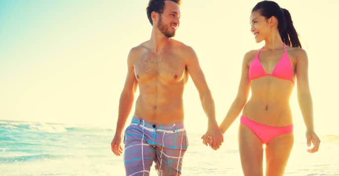 A young couple in swimsuits holding hands while walking on the beach