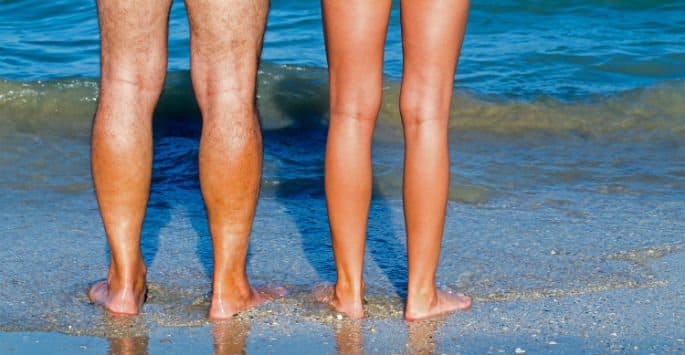 A couple's bare legs standing at the edge of the ocean