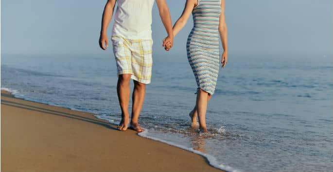 A couple holding hands while walking on the ocean's edge