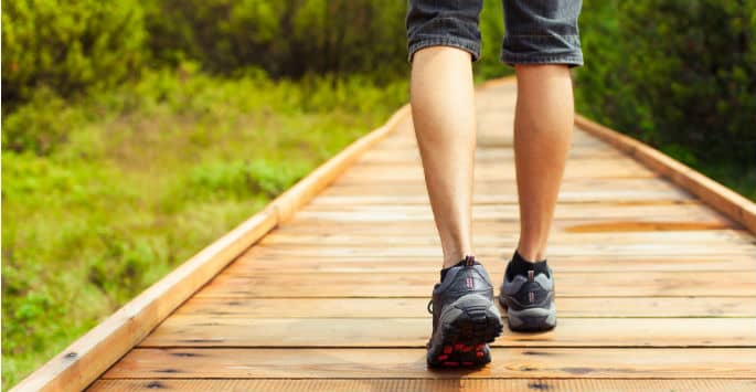 Man's legs in sneakers walking in a nature preserve on a wooden-planed path