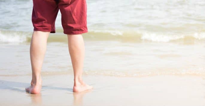 The back of a man's legs in red shorts standing at the edge of the beach