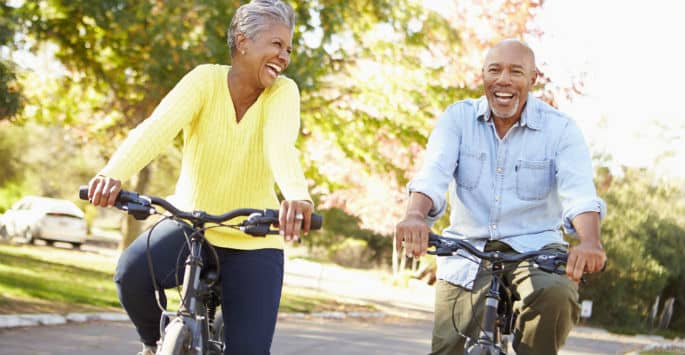 An active older Black couple riding bikes in a residential neighborhood