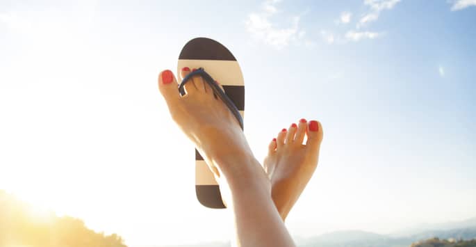 One flip-flop on a pair of raised red-toenailed feet pointed up towards the sky