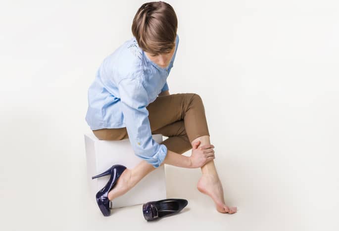 A short-haried lady in a blue oxford and navy pumps rubs her painful leg