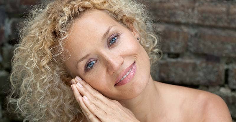 Curly-haired blonde woman with tilted head with a brick wall background